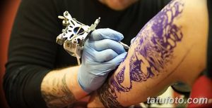 Фото тату: мастер наносит татуировку с использованием фиолетовых и синих оттенков на руку. Крупный план процесса татуирования.